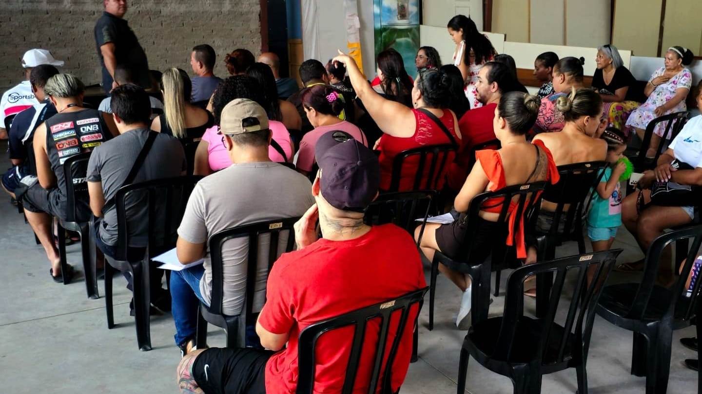 Moradores sentados com fichas em mãos acompanham uma reunião do programa habitacional na sede do Instituto AMEAS.