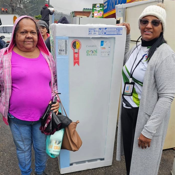 Moradora recebe um refrigerador em ação de apoio habitacional, ao lado de uma voluntária.